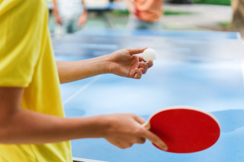 Boy playing ping pong outside during summer sunny day